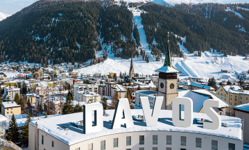 Ein Bergpanorama mit Häusern, Schnee und Wäldern, auf einem Schrfitzug steht Davos.