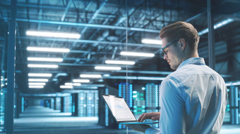 Mann steht mit seinem geöffneten Laptop in einem Datenzentrum.