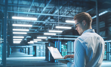Mann steht mit seinem geöffneten Laptop in einem Datenzentrum.