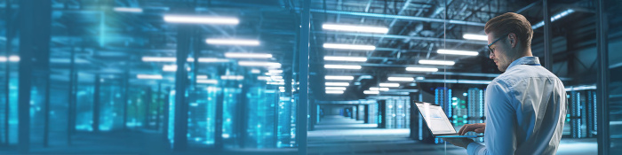 Mann steht mit seinem geöffneten Laptop in einem Datenzentrum.