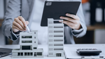 Tablet, Gebäudemodelle und Finanzunterlagen stehen für digitale Analyse im Immobilienbereich.