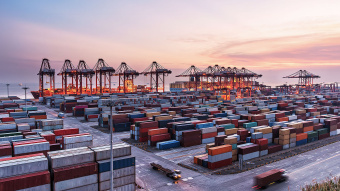 Hafenkräne in einem großen Hafen, dahinter Meer und Containerschiffe. Fokus "Restoring America's Maritime Dominance".