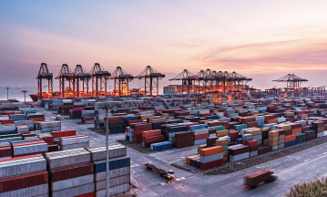 Hafenkräne in einem großen Hafen, dahinter Meer und Containerschiffe. Fokus "Restoring America's Maritime Dominance".