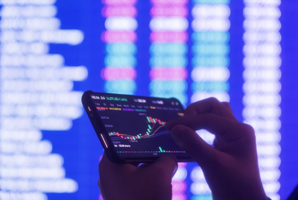 DLT Pilot Regime, digitale Kapitalmärkte, Hände halten Smartphone, auf dem Aktienkurse abgebildet sind