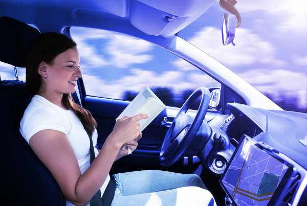 Fahrerin liest Buch beim Autofahren, Wer gestaltet die Zukunft der Kfz-Versicherung?
