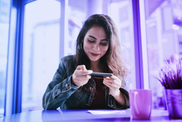 Junge Frau tätigt eine Überweisung mit ihrem Smartphone, Symbolbild für Instant Payments (Echtzeitüberweisungen): So setzen Banken die neuen Pflichten richtig um