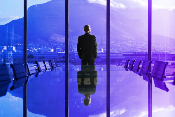 Mann blickt durch große Fenster eines Konferenzsaals auf die Berge, Symbolbild für Vision Kreditprozesse 2030
