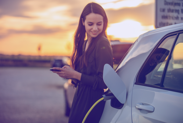 Frau lehnt an Elektroauto, das an der Ladestation lädt