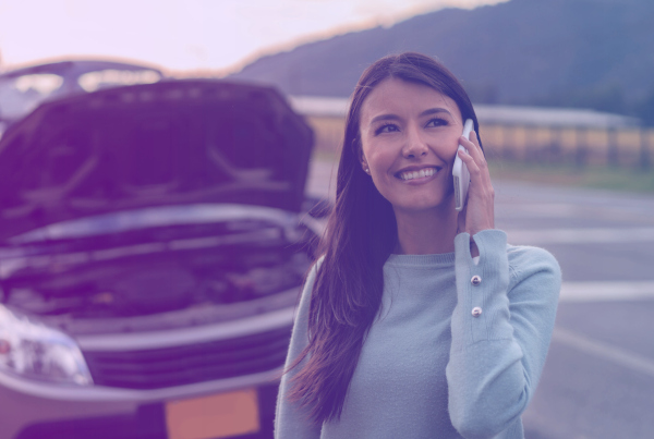 Frau hat Autopanne und telefoniert lächelnd
